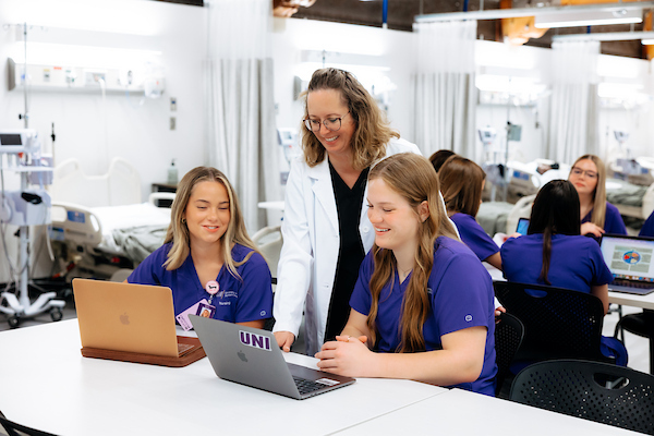 Nursing professor helping two students on laptops