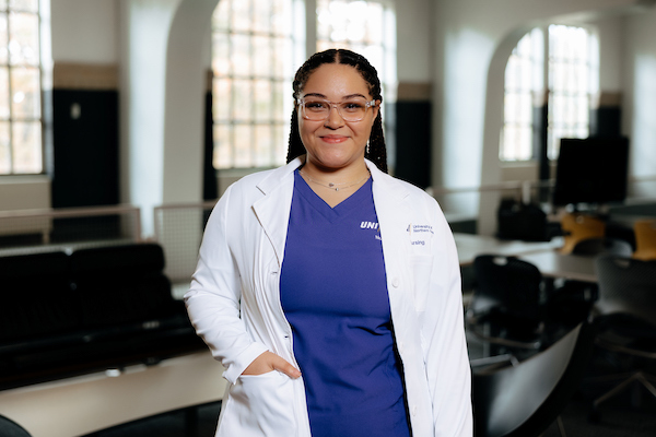 Nursing student in her purple scrubs and white coat